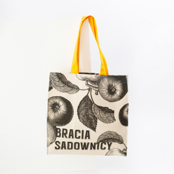 Natural cotton tote bag with Bracia Sadownicy branding, illustrated apples and yellow fabric handles.